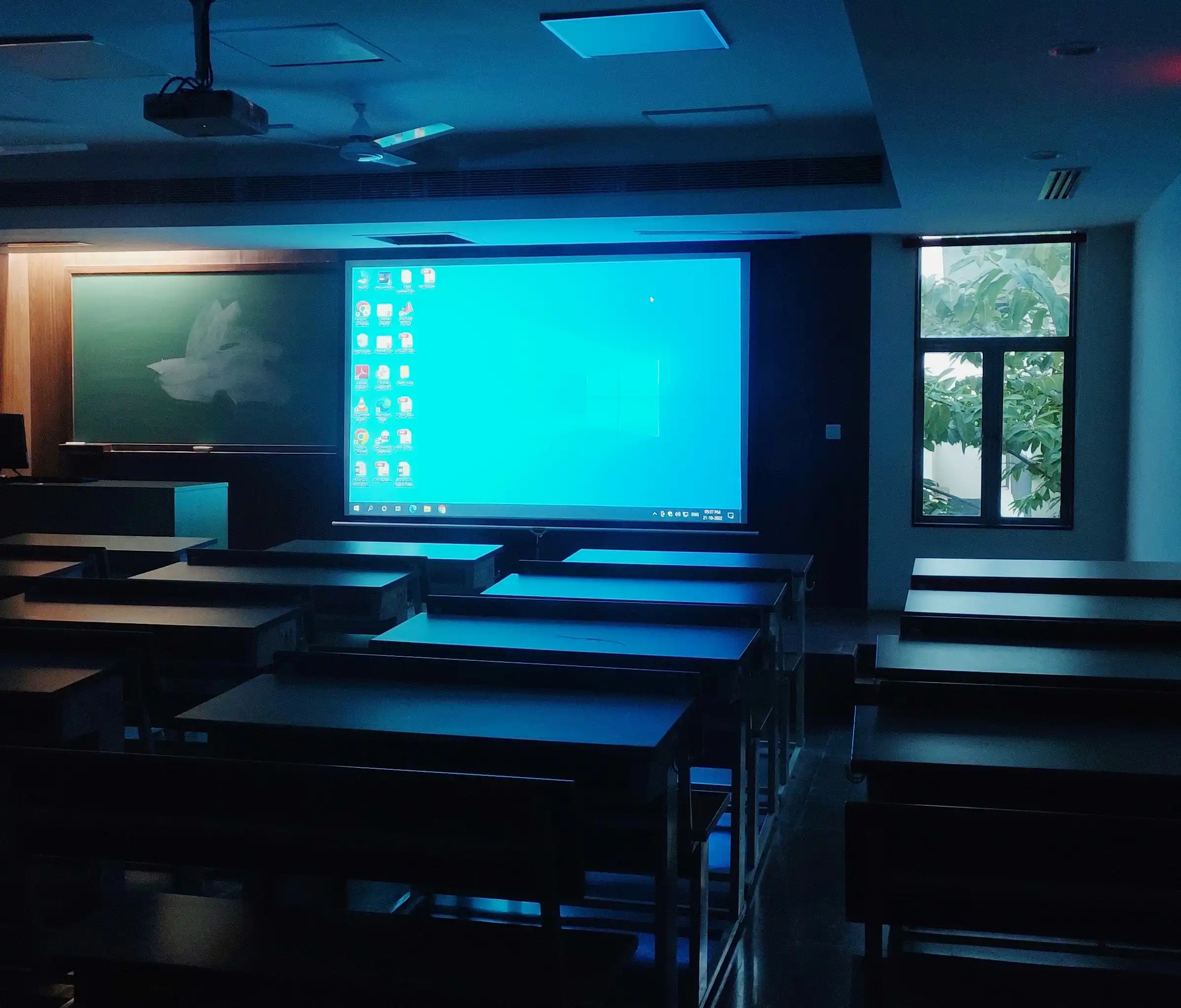 An empty university classroom with a projector illuminating the back wall in blue light